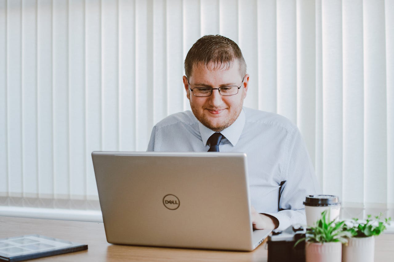 Business professional working on laptop at office desk with coffee and plants.